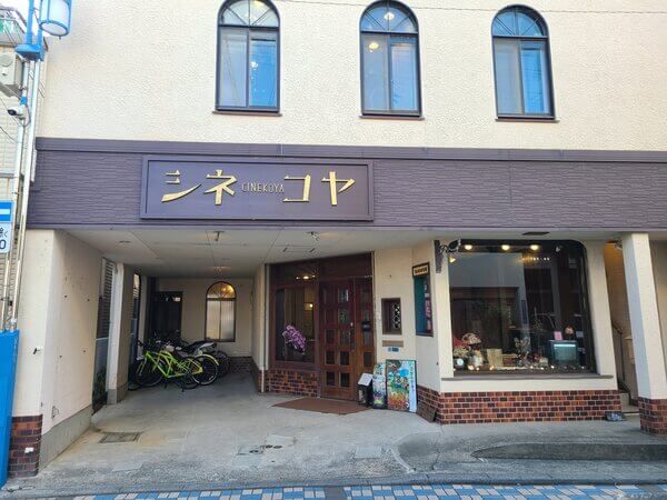 The front of the theater, a cream-colored two-story building with "Cinekoya" written in golden katakana above the entrance.